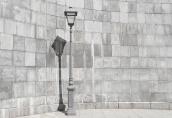 Gray lamppost against grey stone wall. Shadow from a lamppost on a wall on a sunny day. Simple urban background.