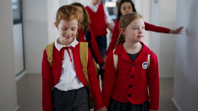 Happy schoolgrirl with Down syndrome in uniform walking in scool corridor with classmates.