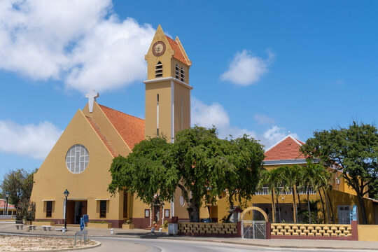 St. Bernard Church (Parokia San Bernardo) Catholic Church in Kralendijk, Bonaire, Caribbean Netherlands. Yellow church with cross, tall clock and bell tower, statue of St. Bernard in a brick niche.