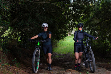 Two latin women cyclists pushing their bike down a mountain trail