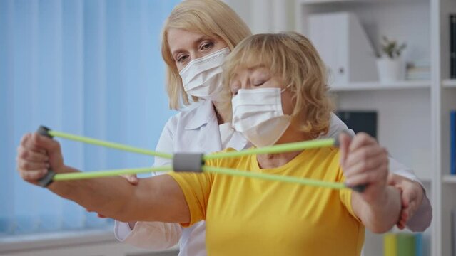 Physiatrist in mask helping her patient do recovery exercises, physiotherapy