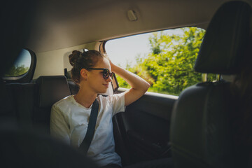 Young woman sitting in the car in the back seat wearing a seat belt looking out the window