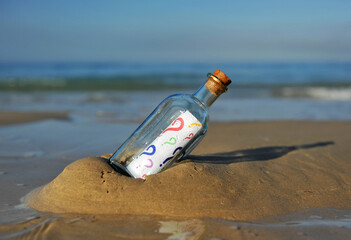 Concepto de incertidumbre. Botella en la playa con preguntas de colores en su interior. Incógnitas sobre el futuro