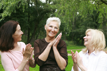 Women friends in the park celebrate a birthday. Clap your hands, congratulate, rejoice. Happy summer day.