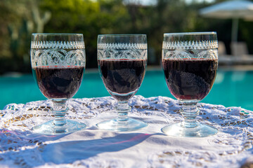 3 bardzo ładnie zdobione kieliszki z czerwonym winem stojące na tacy na tle basenu - obrazy, fototapety, plakaty