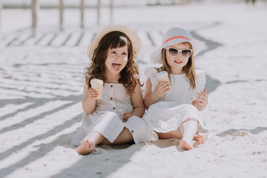 Beautiful little girls in white dress and hat eating ice cream on beach in summer time