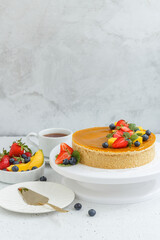 Mango cheesecake decorated with berries, mango slices and flowers on a stand. Vertical photo