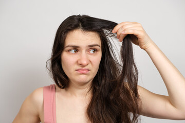 Naklejka premium A beautiful brunette woman without makeup with dirty oily hair holds her hands on her head with a dissatisfied look