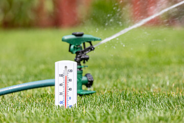 Thermometer with lawn sprinkler watering grass in yard. Drought, water conservation, hot weather...
