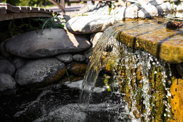 the waterfall flows down the stones in the sun