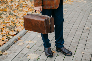 Man with carpetbag in jacket stands in alley of autumn park
