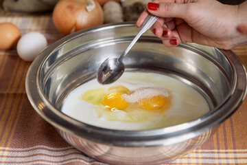 Woman hand holding spoon over bowl of broken eggs..
