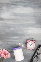 women health concept. medicine, health care style. copy space. white plastic bottle with pills, flowers, glasses and clock on blue wooden background. 