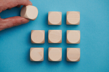 Nine wooden cubes on a blue background standing on top of each other in three rows. The fwmale hand adds the upper left cube, free space for letters, numbers, symbols
