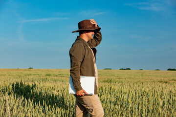 Naklejka na ściany i meble Farmer in hat with laptop computer on wheat field