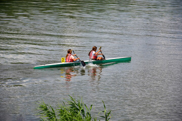 Two young girl athletes in life jackets are sailing canoe on river, controlling oars. Active outdoor sports training. Back view. Copy space. Chisinau, Moldova - July 2021