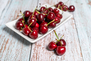 Fototapeta na wymiar white plate with red cherries on wooden table. Seasonal fruit concept