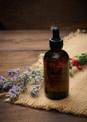 A glass brown bottle with a pipette and a bouquet of lavender on a brown wooden table.