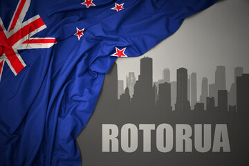 abstract silhouette of the city with text Rotorua near waving national flag of new zealand on a gray background.