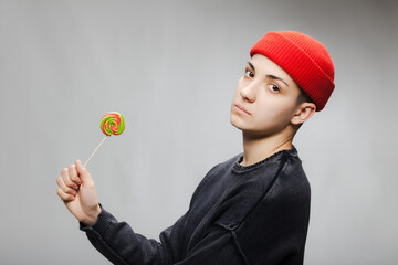 Girl with short hair and a lollipop wearing blouse and red hat against gray background. .