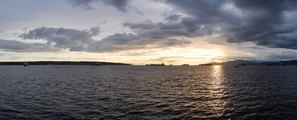 Big Container Ship parked in Burrard Inlet on the West Coast of Pacific Ocean. Colorful cloudy sunset sky. Vancouver, British Columbia, Canada. Panorama Nature Background