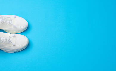 White textile sneakers on a blue background, top view