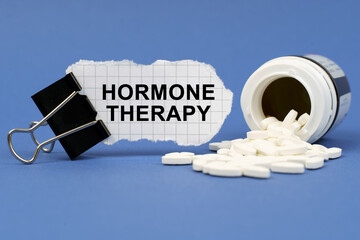 On the blue surface lies a jar of pills and a clip with paper on which is written - HORMONE THERAPY