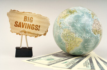 On a gray surface, a globe, dollars and a cardboard plate with the inscription - BIG SAVINGS
