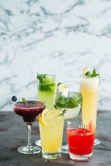 Six summer refreshing cocktails with lemon and mint, vegan beverages on white marble textured table, heathy lifestyle and diet