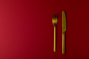 Gold cutlery on the red background. Fork and knife on the red backdrop.