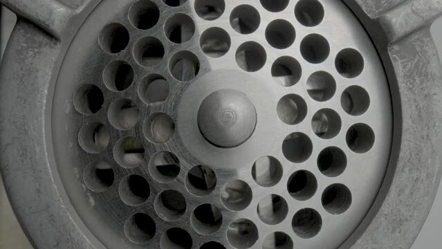 Empty stainless meat grinder close up. Rotation of the knife with four blades and the grating with holes through which the meat passes. Metal electric meat grinder in progress.