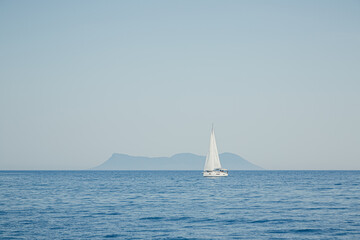 Fototapeta premium single sailboat on the sea in front of an island