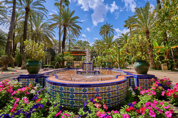 Fountain inside the Palmeral de Elche surrounded by flowers and palm trees. In the municipal park of Elche, Alicante, Spain