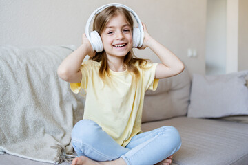 A happy little girl listening music sitting on the sofa in living-room.