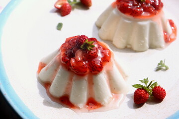 a sweet dessert of cream jelly with a berry confiture of strawberries close-up on a plate.