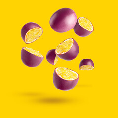 Passion fruit. Pieces of flying fruit. Purple fruits with yellow seeds flying in the air, isolated on a yellow background.