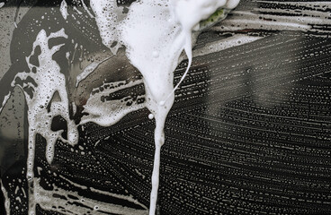 Background, texture of the black surface of a metal car door in white soapy foam after washing. Photo of shampoo streaks.