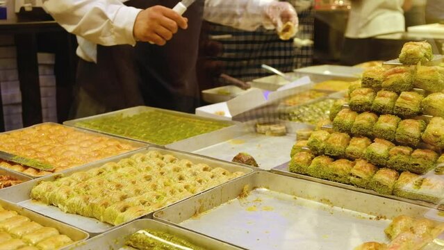 Stacks of baklava at foreground and hands of unrecognizable seller serves customers at traditional turkish delights shop. Showcase of turkish confectionery