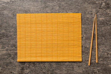 Two chopsticks and bamboo mat on cement background. Top view, copy space