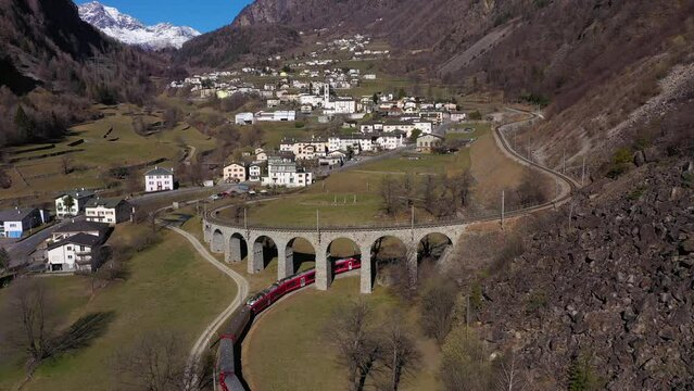 Train on Brusio Spiral Viaduct in Switzerland on Sunny Day. Bernina Railway. Swiss Alps. Aerial View. Drone Flies Forward