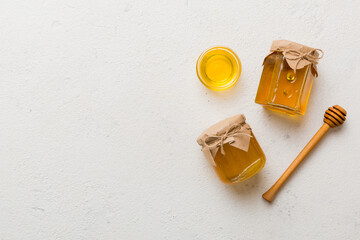 Glass jar of honey with wooden drizzler on colored background. Honey pot and dipper high above. Top...