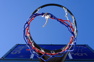 Basketball hoop and net against a blue sky. Urban youth game. Low angkle view below the hoop net....