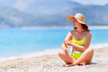 Young girl applying sunscreen lotion while sunbathing and relaxing on beach by the sea in sunny summer day. Sun protection