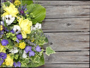 Strauss aus echten Blüten mit blauen Glockenblumen und gelben Rosen, weissen Matrikaria, Leinkraut und Funkienblättern vor Hintergrund aus Holzdielen