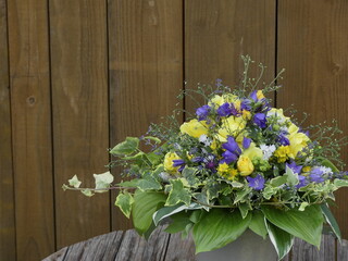 Strauss aus echten Blüten mit blauen Glockenblumen und gelben Rosen, weissen Matrikaria, Leinkraut und Funkienblättern vor Hintergrund aus Holzdielen