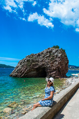 Young woman in front of beautiful rocks on pebble public stone beach. Rafailovici esort towns. Mountenegro.