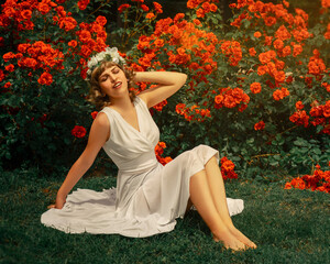 Mujer de vestido blanco sentada en medio de un jardín de rosas rojas , hada en medio de la...