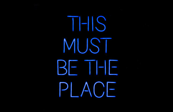 Isolated blue neon sign on black background that says 'this must be the place' 
