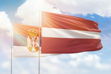 Sunny blue sky and flags of latvia and serbia