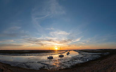 Naklejka premium Sunrise with sailing boats moored on Mount lake with Hurst lighthouse in the distance with mudflats exposed with the low tide at Hurst spit. Milford on Sea, Hampshire, UK. 